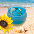 Blue and yellow candle  adorned with turtle, seashell, quartz, amazonite, aventuring on a beach setting with a sunflower.