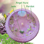Purple lilac candle in a beautiful vessel, with floral and greenery elements on a blurred natural background. Adorned with Jade, Angel Aura Heart and Peridot sprinkles.