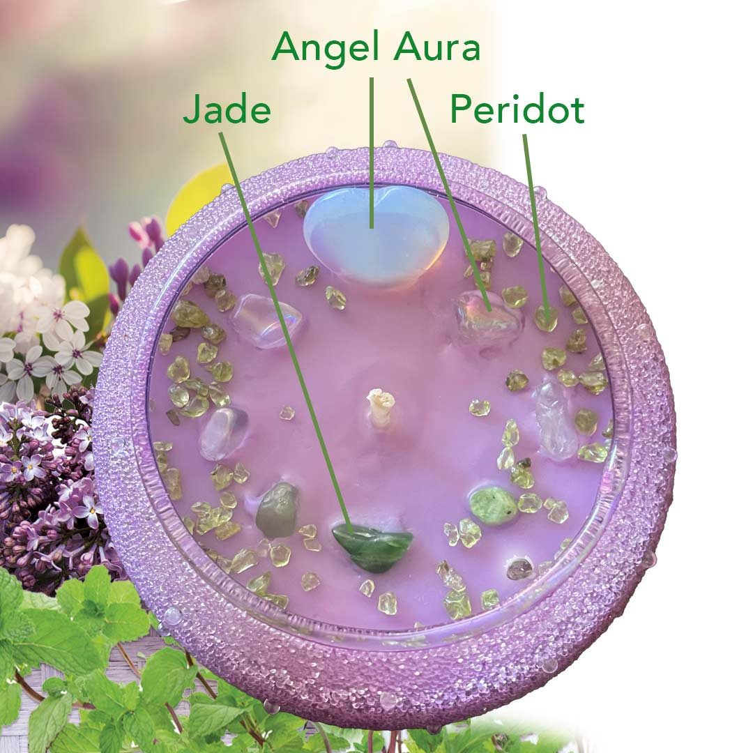 Purple lilac candle in a beautiful vessel, with floral and greenery elements on a blurred natural background. Adorned with Jade, Angel Aura Heart and Peridot sprinkles.