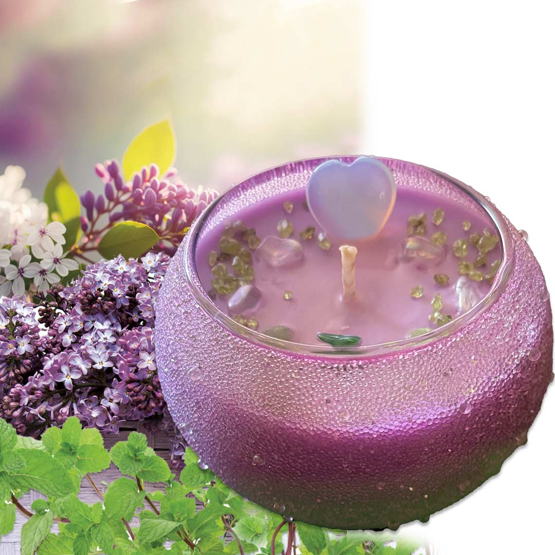 Purple lilac candle in a beautiful vessel, with floral and greenery elements on a blurred natural background.