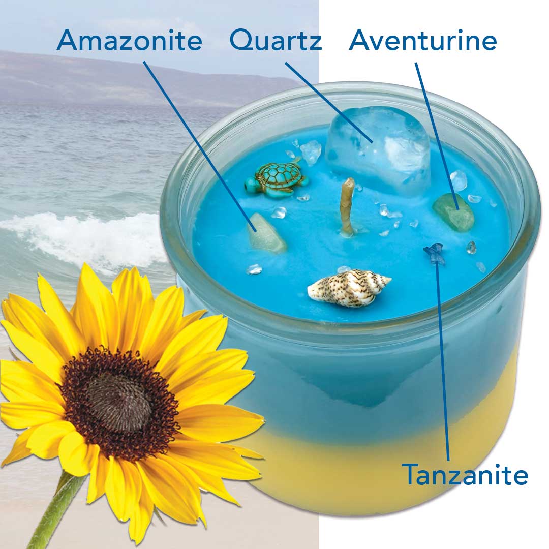 Blue and yellow candle in a jar with decorative elements, adorned with Amazonite, Quartz, Aventurine, Tanzanite, turtle and seashell next to a sunflower, beach in the background.